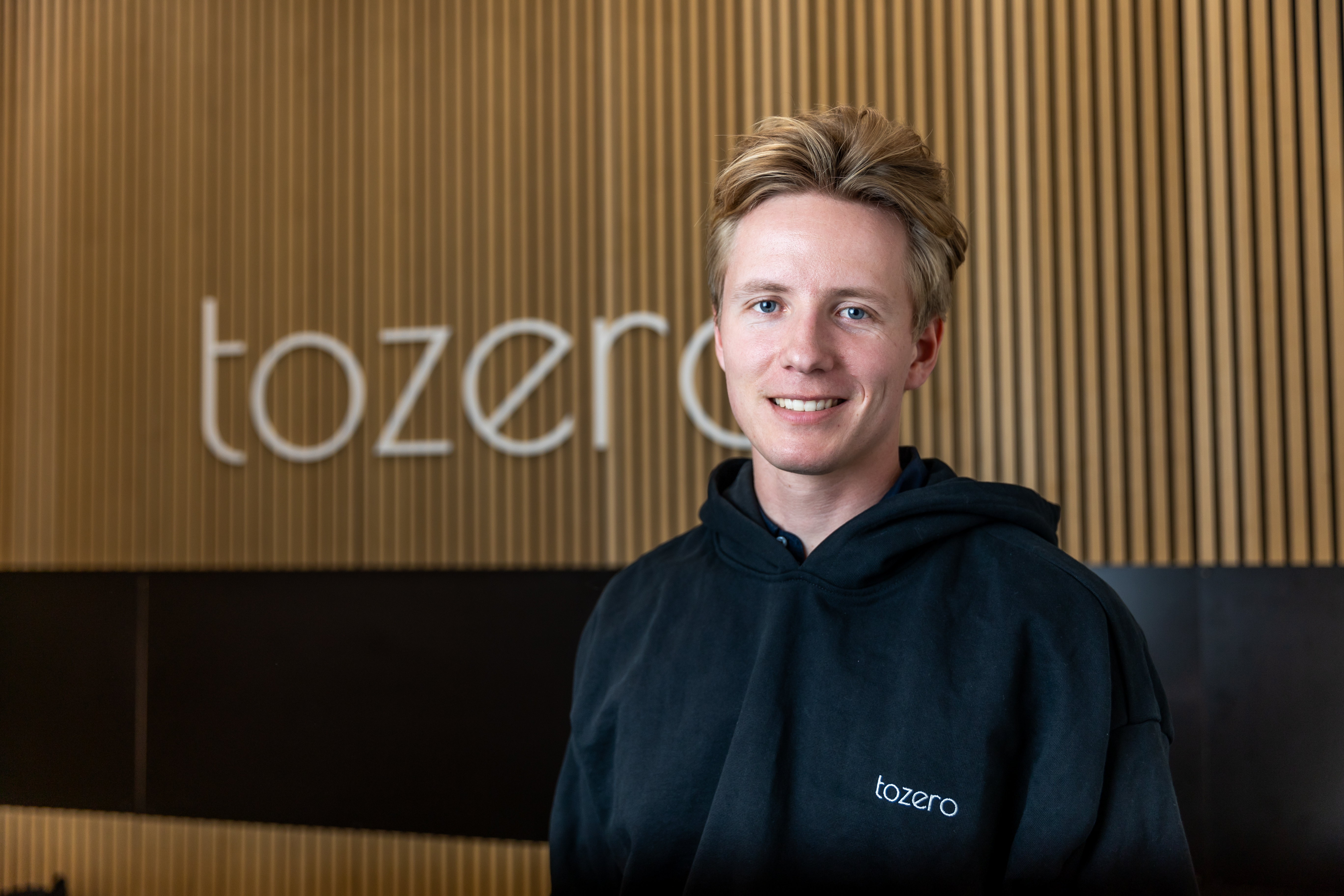 Portrait of Lorenz Kopp standinginfront of the tozero Logo