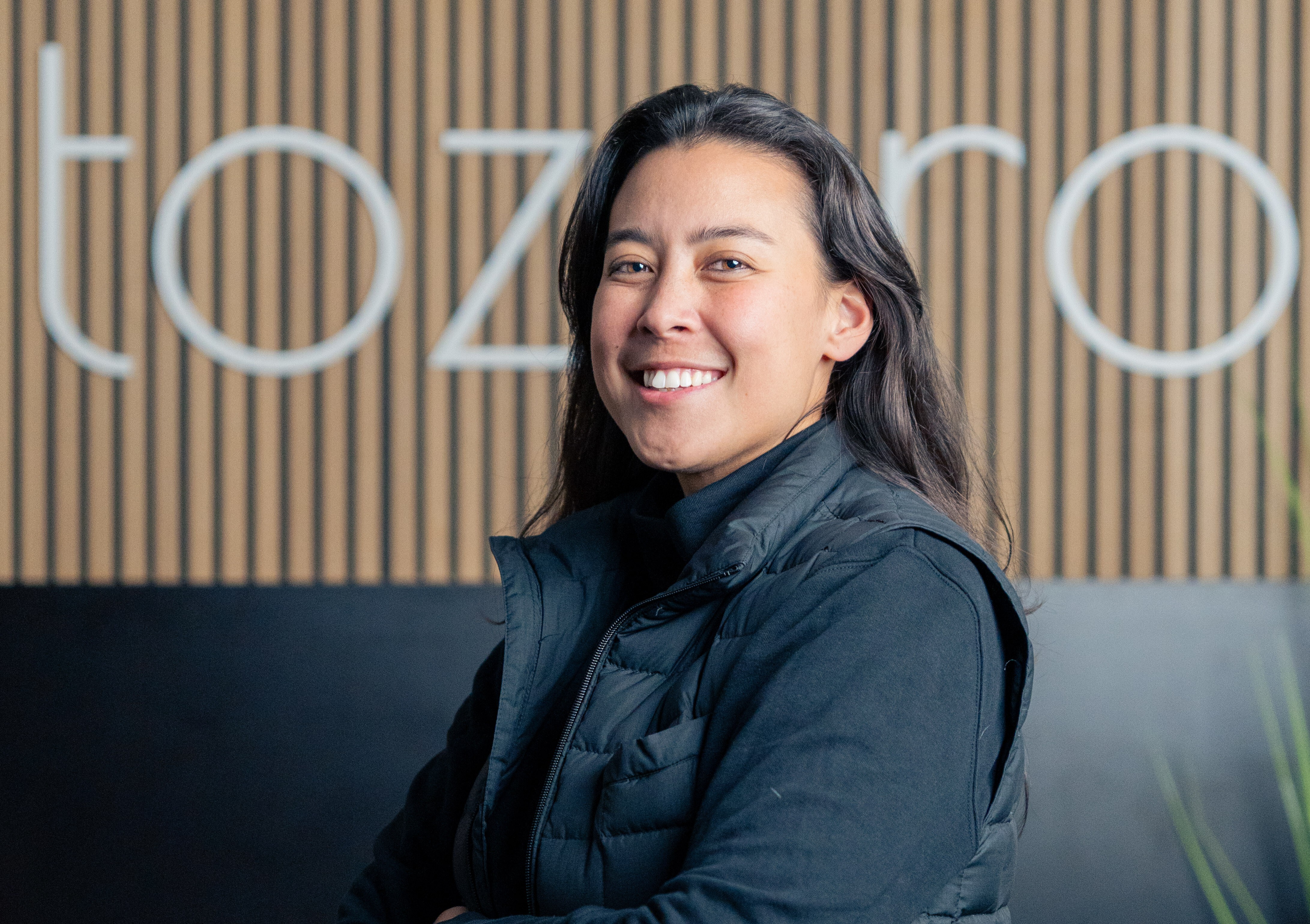 Portrait of Sarah Fleischer standinginfront of the tozero Logo